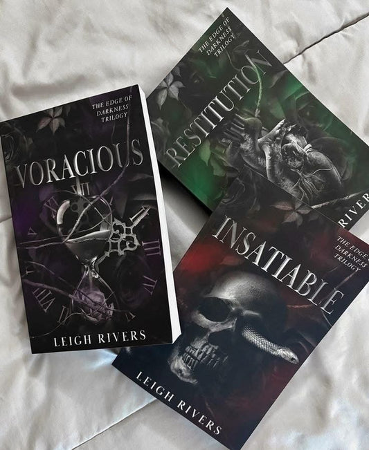 Three books from the 'Vengeful Inhumanity Trilogy' by Leigh Rivers on a textured surface.